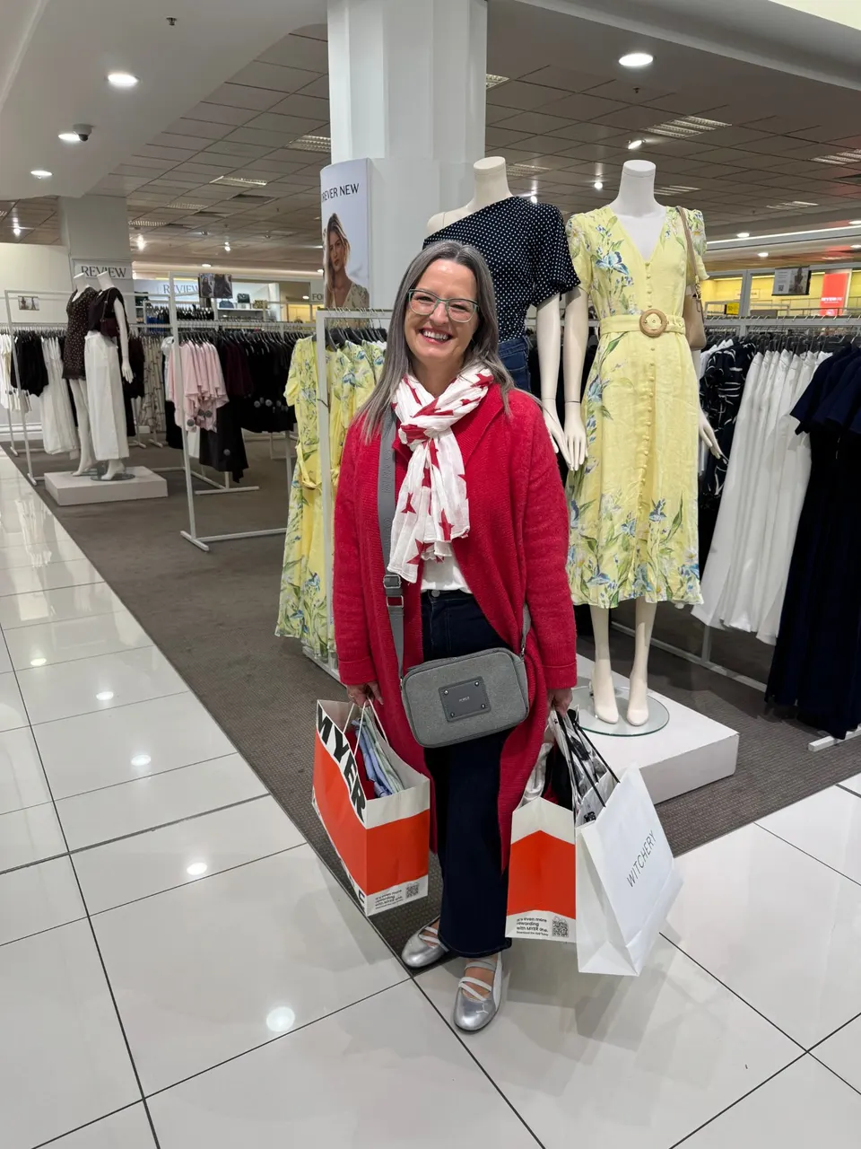 A smiling client in a red cardigan holding shopping bags in a department store