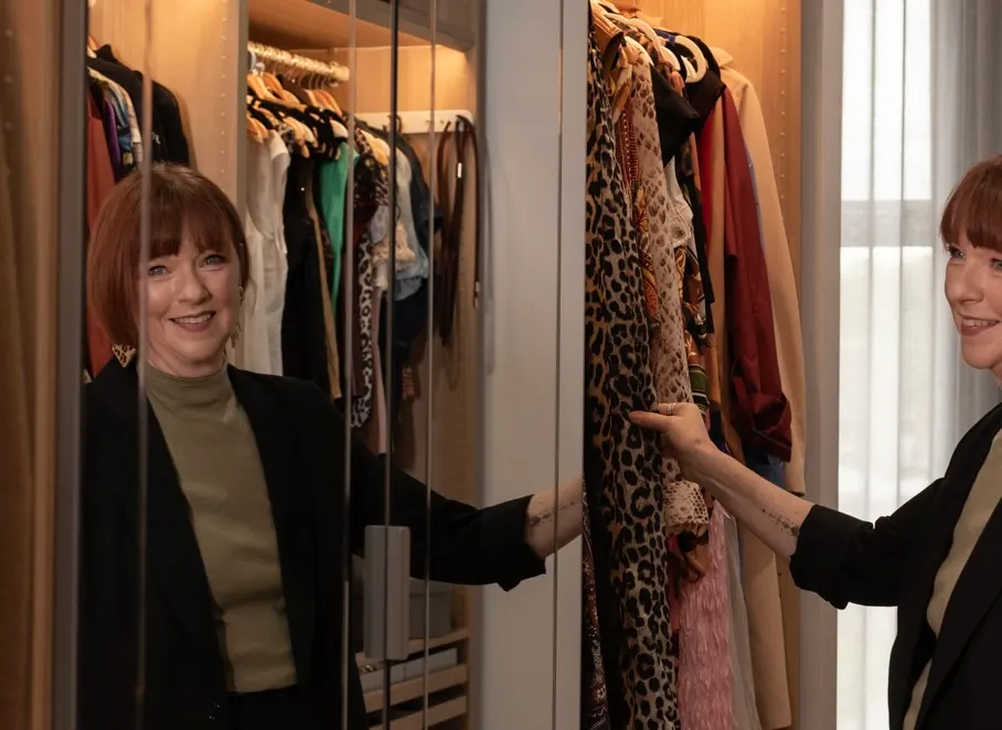 Steph reflected in a wardrobe mirror, smiling as she browses a rail of patterned clothes